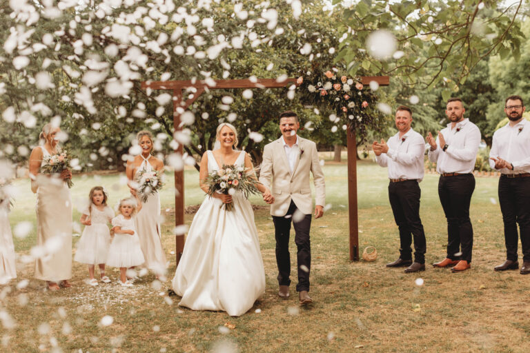 Wedding couple posing with family and friends on a decorative outdoor lawn, bride holding a bouquet - Wedding DJ Canberra