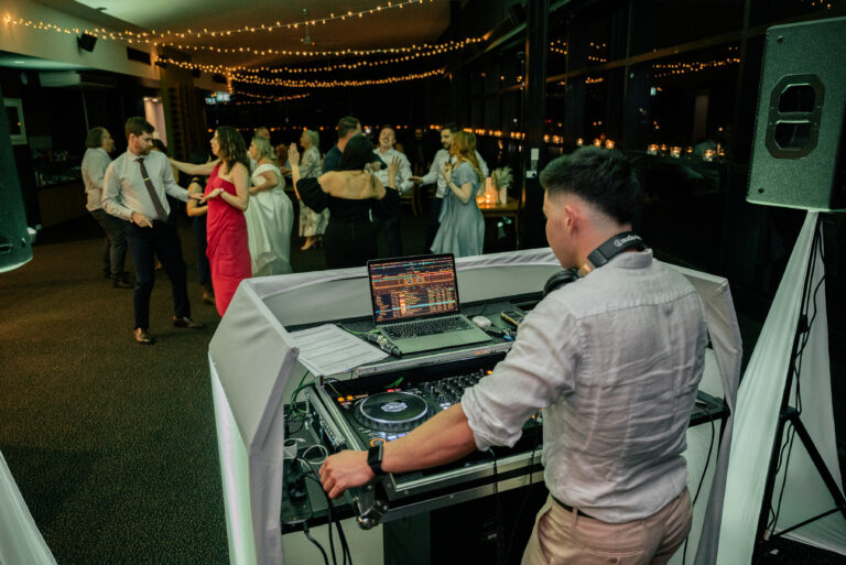 DJ at a night event standing at his desk, playing beats with the DJ system in front of the crowd, wedding DJ Canberra