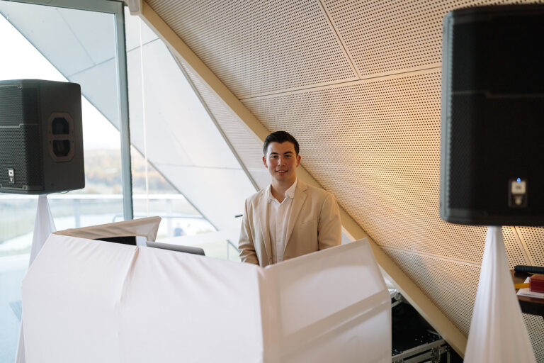 Professional DJ facing the camera sitting on his DJ desk covered with a white sheet at a wedding event - wedding DJ Canberra